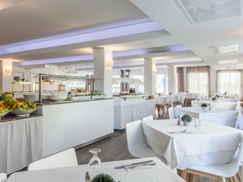 Ein heller, moderner Speisesaal mit rund gedeckten Tischen, weißen Tischdecken und Buffetbereich.