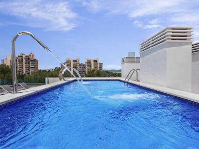 Schwimmbad auf Dach mit klar blauem Wasser, Edelstahlgeländern und Stadtblick im Hintergrund.