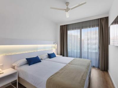 Nowoczesny pokój hotelowy z podwójnym łóżkiem, wentylatorem sufitowym i dużym oknem z zasłonami.