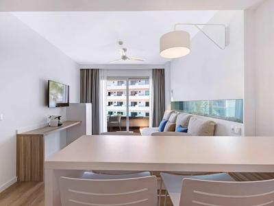 Nowoczesny, jasny pokój hotelowy z przytulnym kącikiem, balkonem i telewizorem.