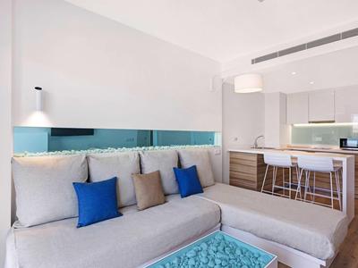 Jasna nowoczesna kuchnia z sofą, niebieskimi poduszkami i wyspą kuchenną z hokerkami.