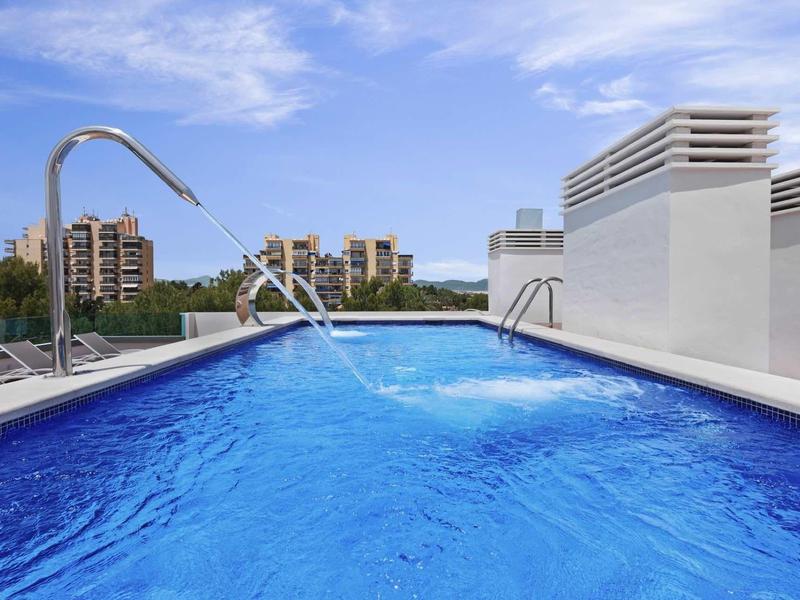 Nowoczesny basen na dachu z wodospadami i widokiem na budynki.