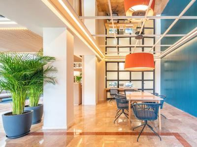 Nowoczesne wnętrze z niebieską ścianą akcentową, stolikami, krzesłami i dużą rośliną doniczkową.