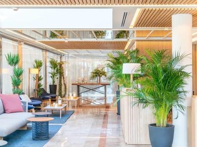 Jasne lobby hotelowe z nowoczesnymi meblami, roślinami i drewnianymi elementami sufitowymi.