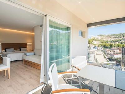 Balkon mit weißen Stühlen und Tisch, Blick auf Stadt und Hügel, angrenzend an modernes Schlafzimmer.