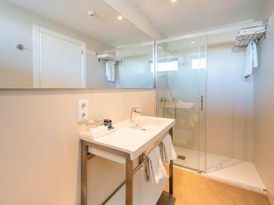 Helles Badezimmer mit weißem Waschbecken, großem Spiegel und Glas-Duschkabine, minimalistisch gestaltet.