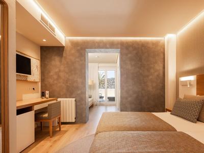 Modernes Hotelzimmer mit zwei Betten, grauen Wänden und Blick auf Balkon.