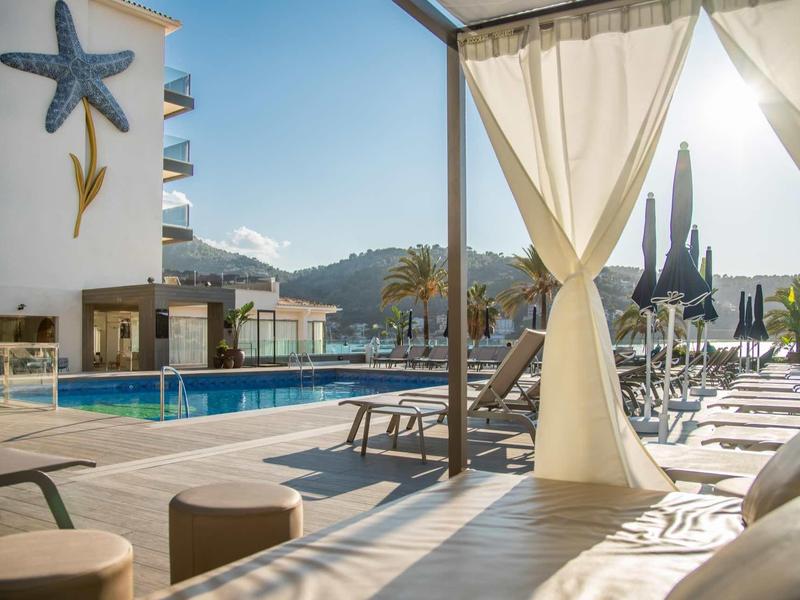 Moderner Poolbereich mit Liegestühlen, Sonnenschirmen und gemusterten Kissen bei klarem Himmel.