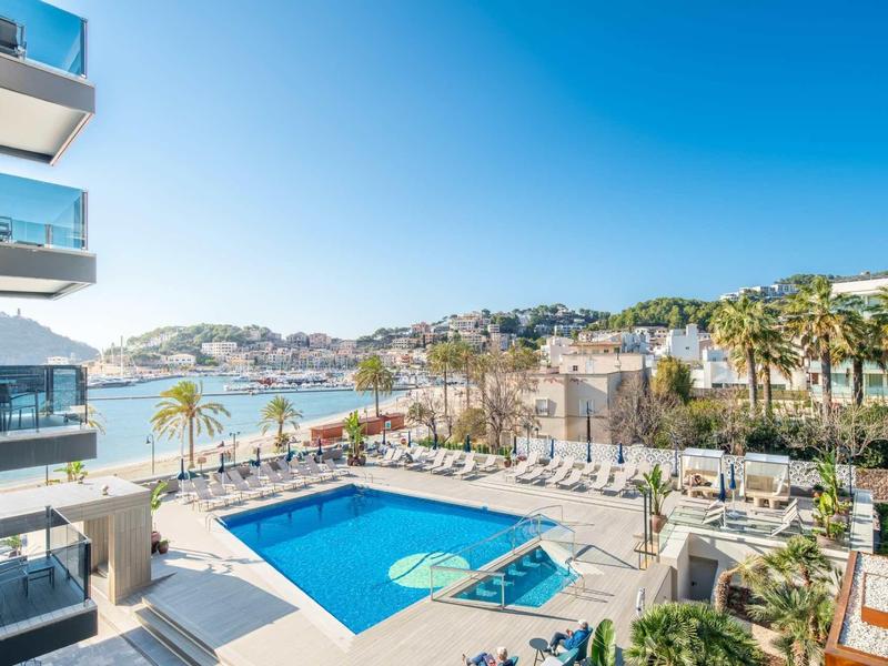 Moderner Poolbereich mit Liegestühlen, Palmen und Blick auf das offene Meer an sonnigem Tag.