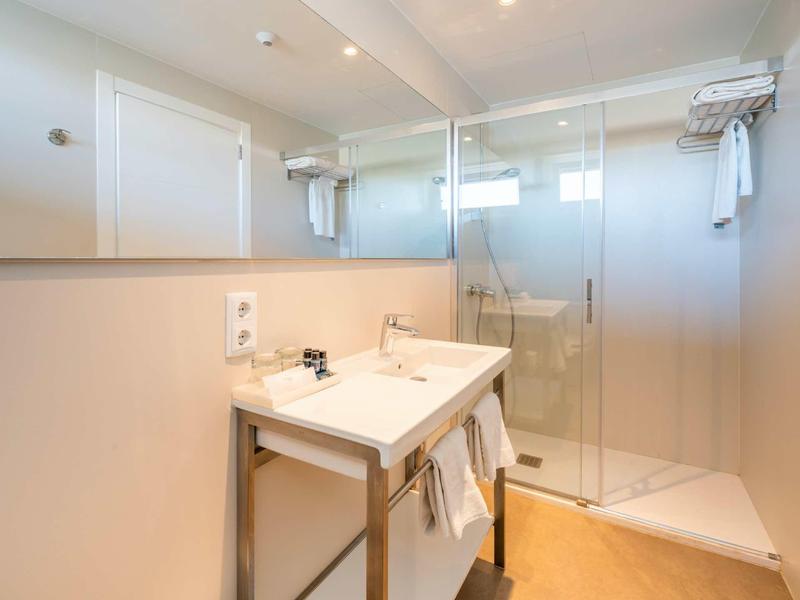 Helles Badezimmer mit weißem Waschbecken, großem Spiegel und Glas-Duschkabine, minimalistisch gestaltet.