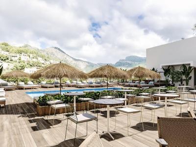 Moderne hotelentree met zwembad, parasols en berglandschap op de achtergrond.