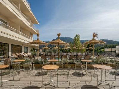 Terras met tafels, stoelen en parasols voor een modern hotelgebouw op een zonnige dag.