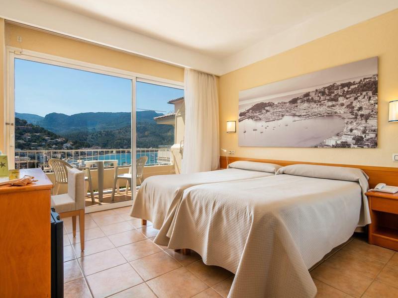 Camera d'hotel accogliente con letto matrimoniale e balcone con vista sulle montagne al tramonto.