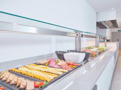 Buffet mit verschiedenen Wurst- und Käsesorten, Schalen und Tellern auf langem weißen Tisch.