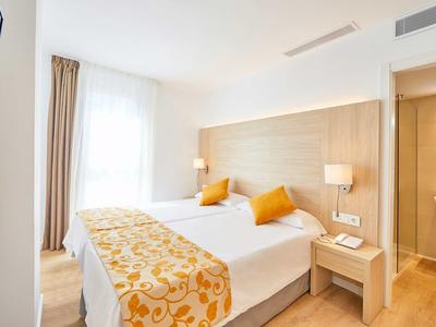 Modernes Schlafzimmer mit zwei Betten, holzfarbenem Kopfteil, gelben Dekokissen und Tagesdecke.