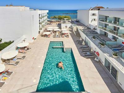 Moderner Außenpool zwischen zwei Hotels mit Liegestühlen und Blick auf das Meer im Hintergrund.