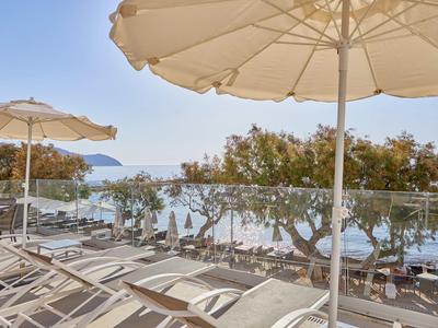 Blick von einer Terrasse mit Liegestühlen und Sonnenschirmen auf das Meer und Bäume.