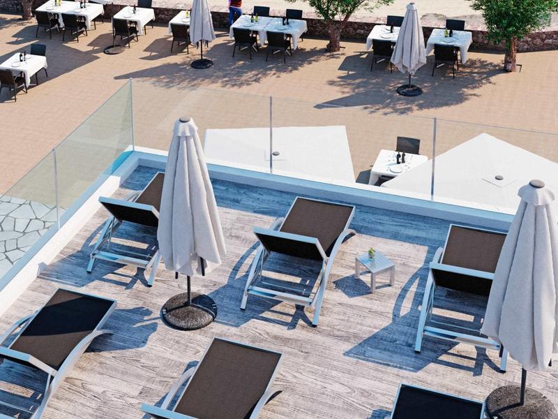 Blick auf Liegen mit weißen Sonnenschirmen und Tischen am Strand neben blauem Meer.