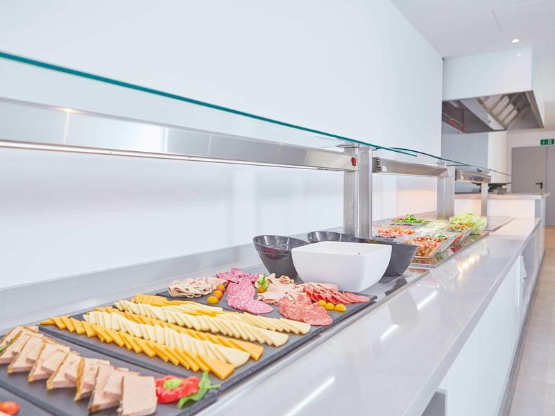 Buffet mit verschiedenen Wurst- und Käsesorten, Schalen und Tellern auf langem weißen Tisch.