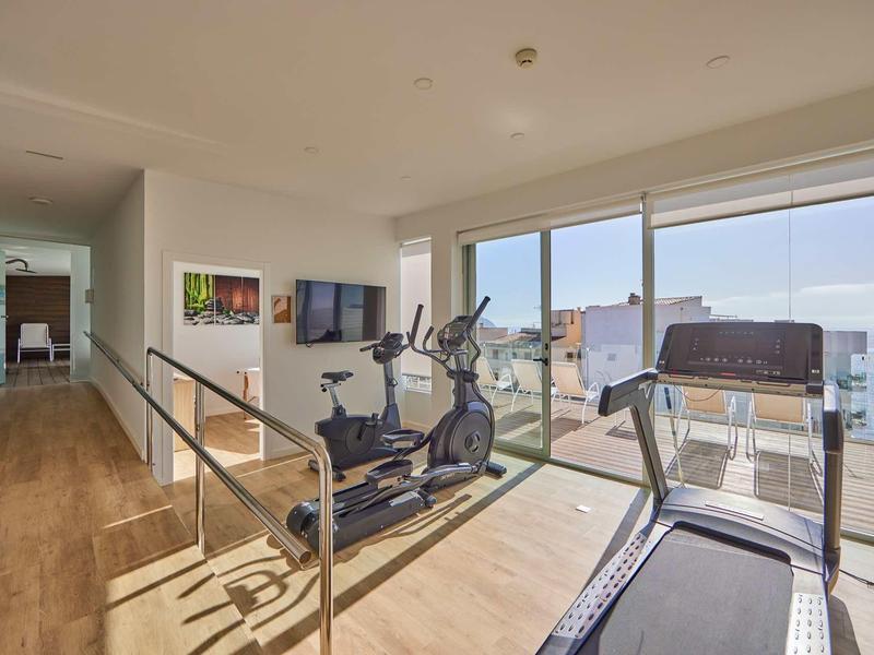 Moderner Fitnessraum mit Laufband, Crosstrainer, Holzfußboden und großen Fenstern mit Meerblick.