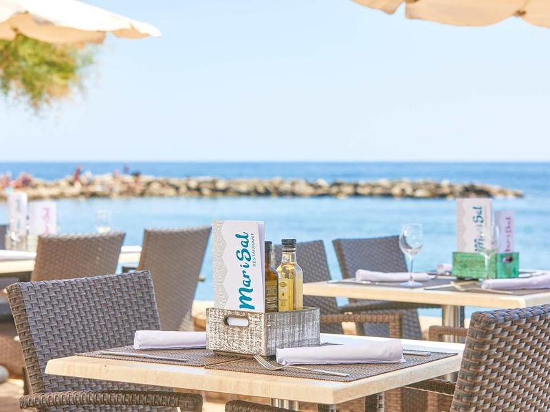 Terrassenrestaurant mit Tischen, Stühlen und Blick auf Meer und bewölkten Himmel.