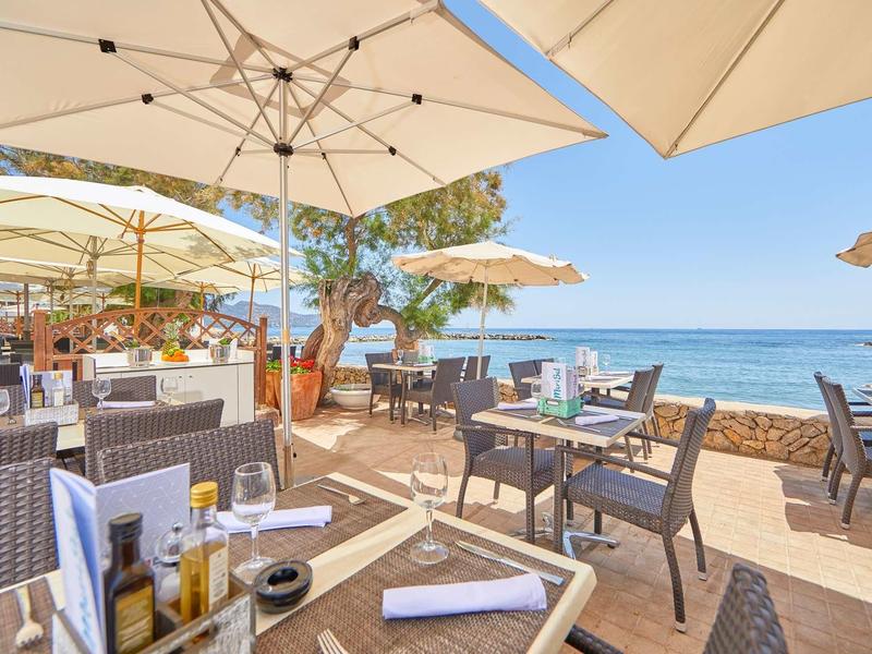 Outdoor-Restaurant am Meer mit Tischen, Sonnenschirmen und blauer Himmel im Hintergrund.
