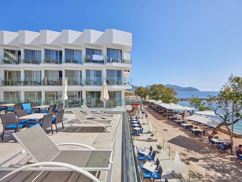 Moderne Hotelterrasse mit Liegestühlen, Sonnenschirmen und Blick auf Strand und Meer.