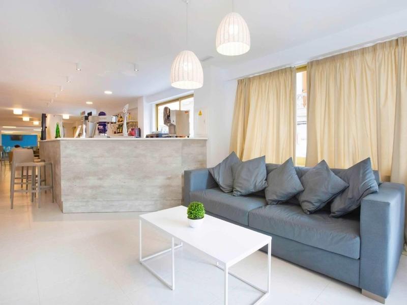 Jasny salon z szarą sofą, białym stolikiem i dużymi zasłonami.