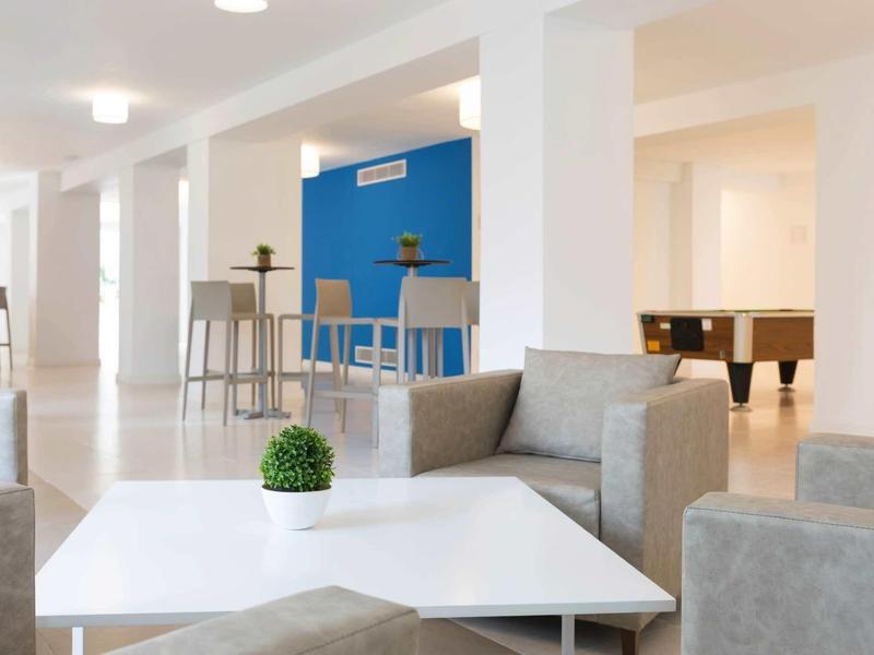 Nowoczesny salon z szarymi fotelami, białym stołem i barem z niebieską ścianą.