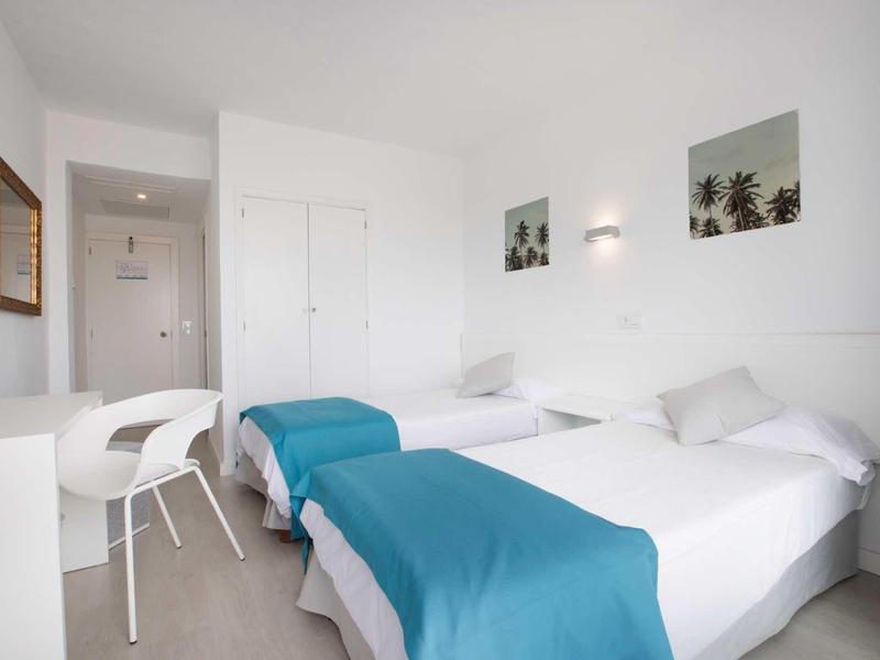 Nowoczesny pokój hotelowy z dwoma łóżkami pojedynczymi, białymi ścianami i niebieskimi narzutami.