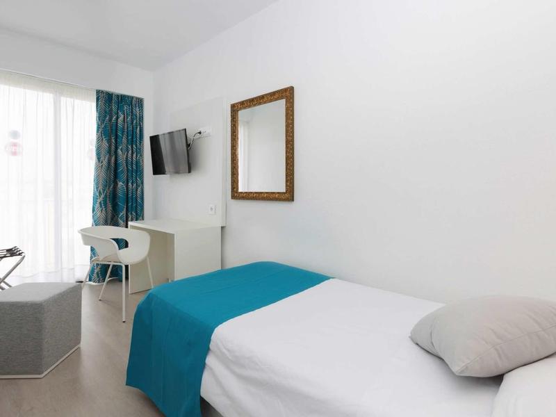 Nowoczesny pokój hotelowy z jednoosobowym łóżkiem, niebieskim narzutem, lustrem na ścianie i telewizorem.