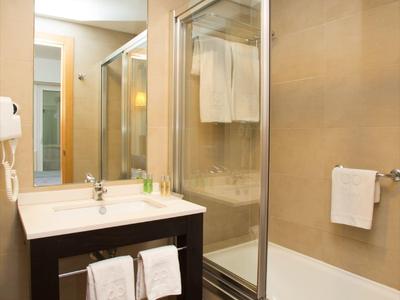 Hotelová koupelna s umyvadlem, zrcadlem a vanou se skleněnými dveřmi sprchy.