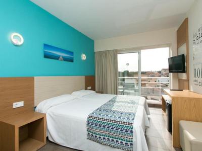 Moderní hotelový pokoj s manželskou postelí, televizí na stěně a balkonem s výhledem na město.