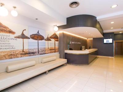 Moderner Hotellobby mit Empfangstresen, hellen Bodenfliesen und Sitzbank unter Strandbild.