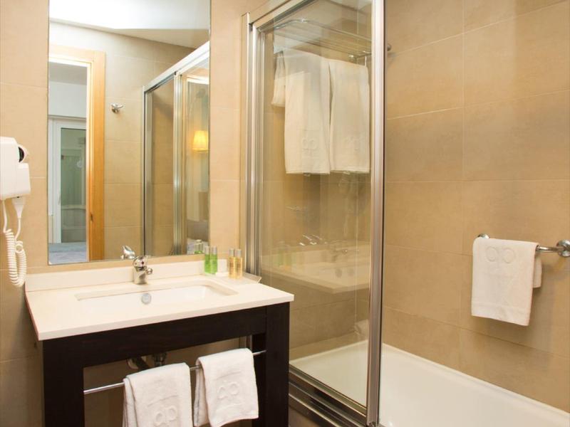 Hotelová koupelna s umyvadlem, zrcadlem a vanou se skleněnými dveřmi sprchy.