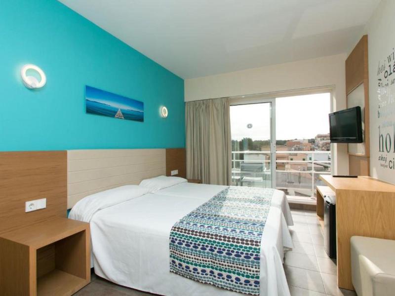 Moderní hotelový pokoj s manželskou postelí, televizí na stěně a balkonem s výhledem na město.