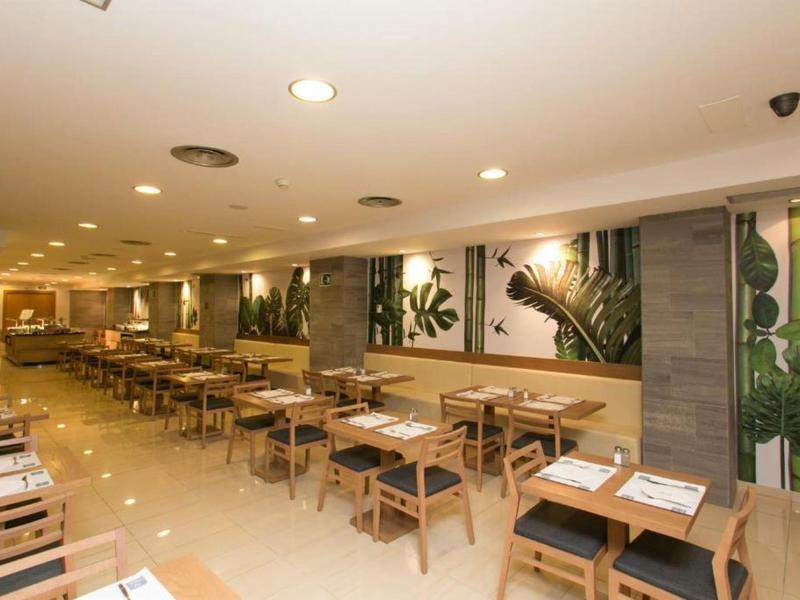 Moderní hotelová restaurace s dřevěnými stoly, světlými stěnami a botanickými nástěnnými dekoracemi.