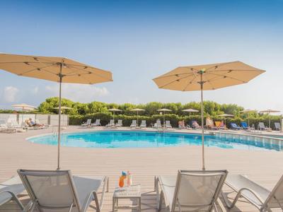 Zwei Liegestühle mit Sonnenschirmen am blauen Pool unter klarem Himmel.