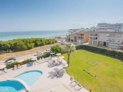 Blick auf ein Schwimmbad mit Liegestühlen, Rasenfläche und Meer im Hintergrund bei klarem Himmel.