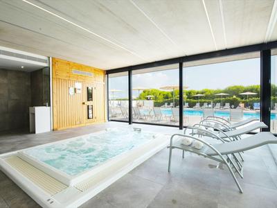 Modern wellness area with jacuzzi and lounge chairs in front of large windows overlooking greenery.