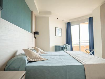 Modern hotel room with two single beds, light walls, and balcony with a view.