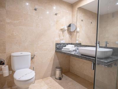 Modern hotel bathroom with toilet, sink on black marble countertop, and glass shower enclosure.