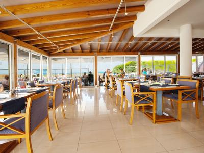 Großes, helles Restaurant mit Holzbalkendecke, Glaswänden und modernen Holztischen und Stühlen.