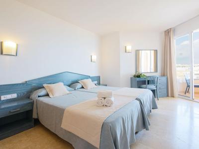 Brightly furnished hotel room with double beds, desk, and access to a balcony.