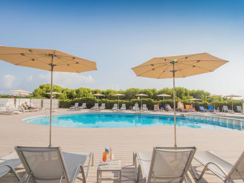 Zwei Liegestühle mit Sonnenschirmen am blauen Pool unter klarem Himmel.