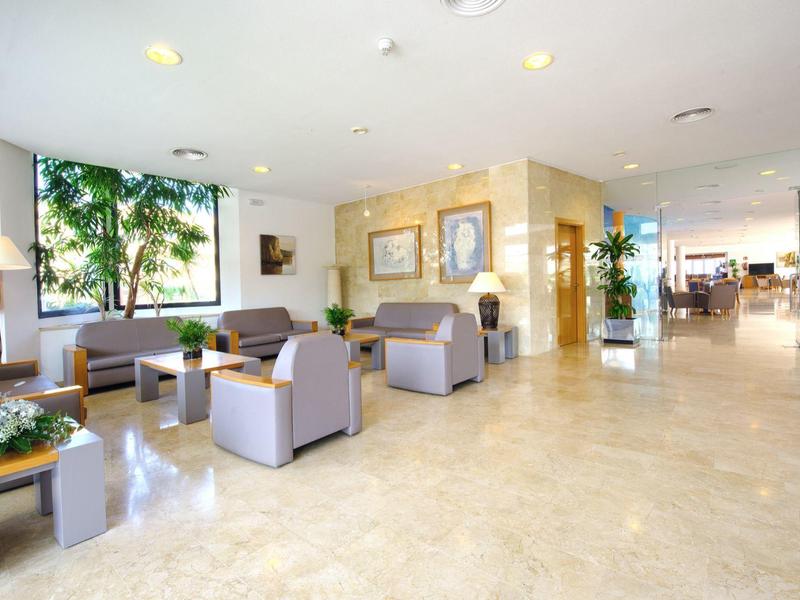 Heller, großzügiger Wartebereich mit grauen Sesseln, Holztischen und großen Fenstern.