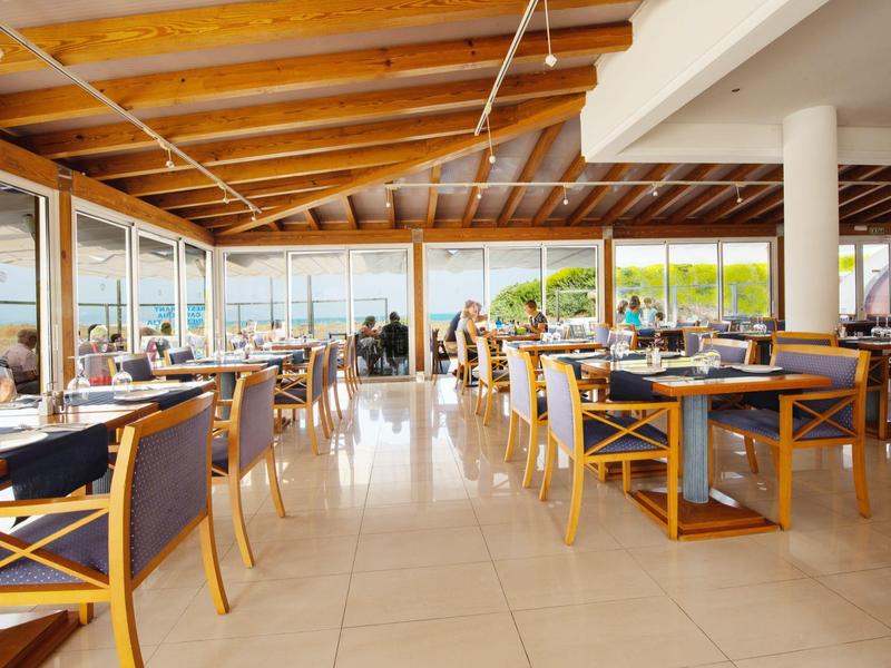 Großes, helles Restaurant mit Holzbalkendecke, Glaswänden und modernen Holztischen und Stühlen.