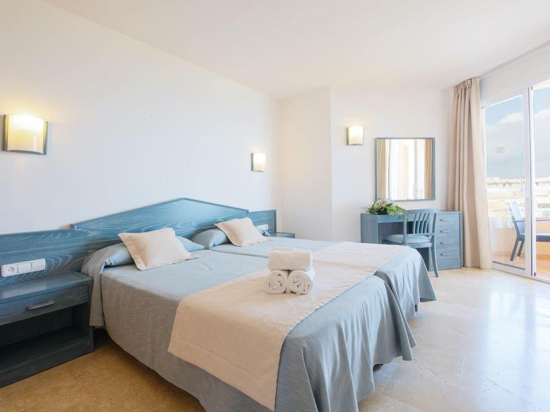 Helles Hotelzimmer mit zwei Einzelbetten, grauer Bettwäsche, Nachttischen und Balkon mit Meerblick.