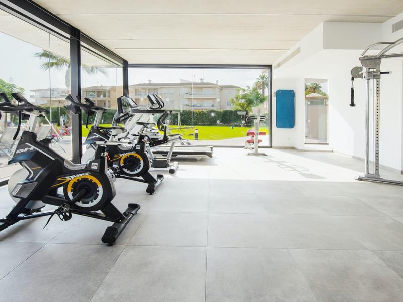 Heller Fitnessraum mit großen Fenstern, mehreren Fahrradergometern und modernem Trainingsgerät.