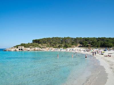 Clear blue sky over a sandy beach with clear sea water and people at the shore.